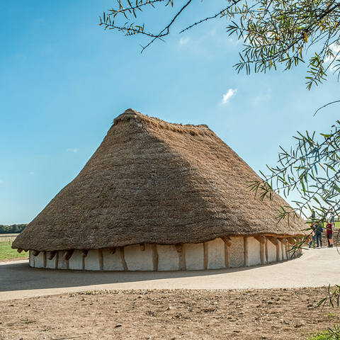 A view of the Kusuma Neolithic Hall at Stonehenge underneath a blue sky.