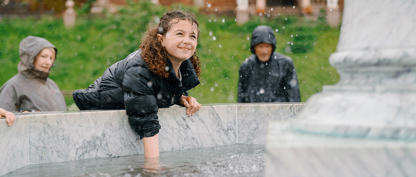 Photo of a child putting their hand in the water at a fountain in the rain at Kenilworth Castle and Elizbethan Garden in Warwickshire