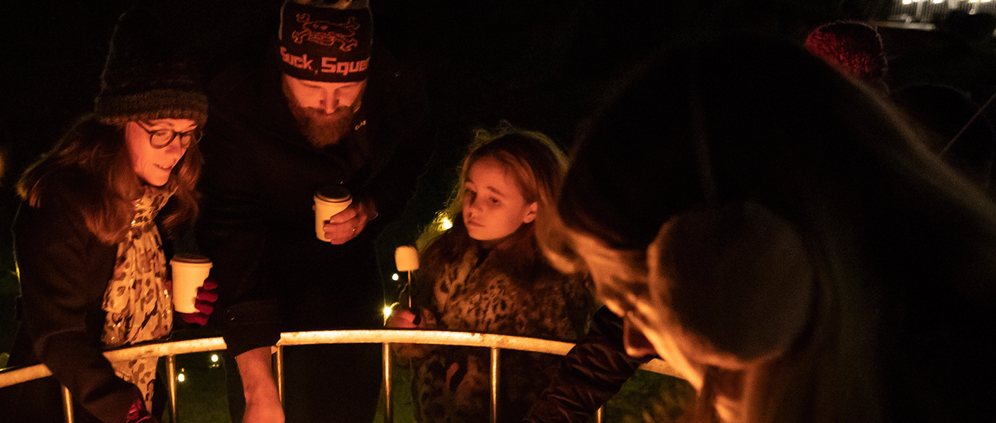 Photo of a group of children and adults standing around a fire pit and toasting marshmallows