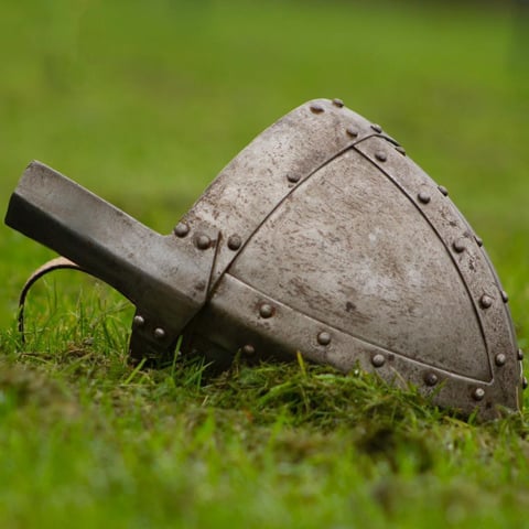 A replica of a medieval helmet laid on the grass.